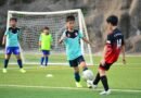 Boys playing soccer during a team training session outdoors on a sunny day.