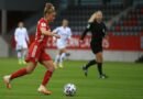 A female soccer player in red uniform dribbles during a match.