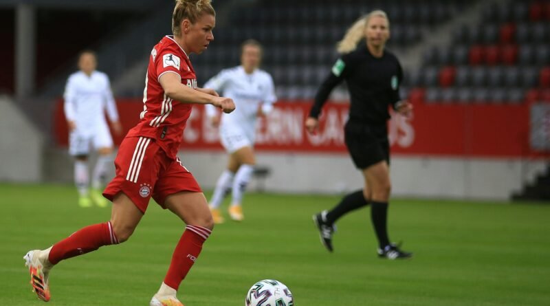 A female soccer player in red uniform dribbles during a match.